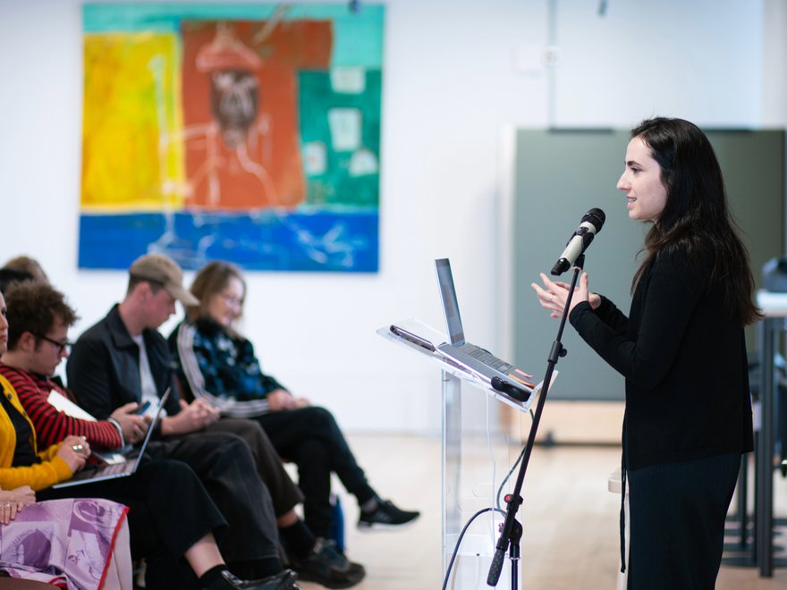 a woman talks at a lecture while people sit and listen