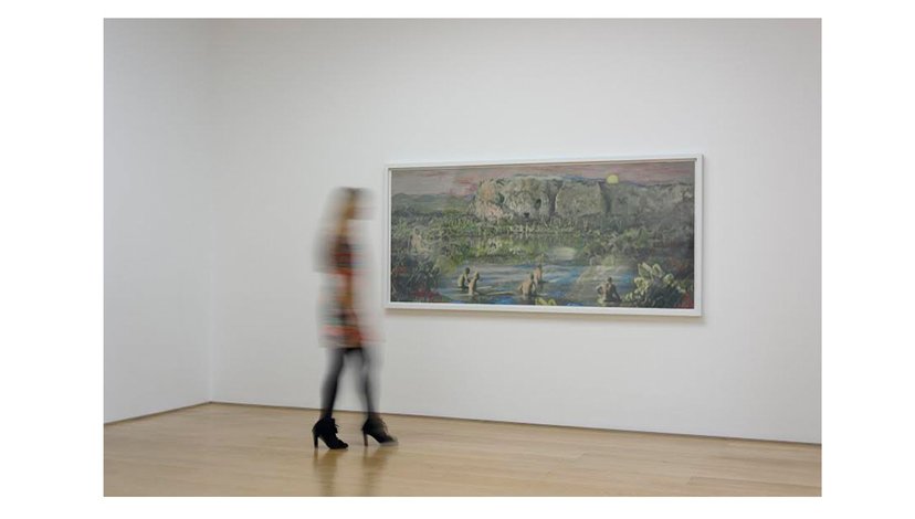 Blurred out figure standing in front of a large landscape painting in a gallery.