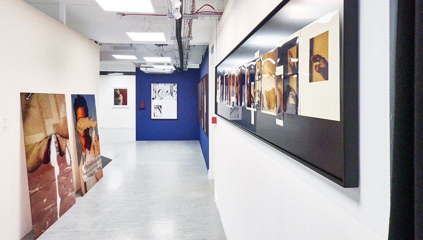 Installation view of exhibition, with large painted canvases hanging in a corridor and propped against a wall.