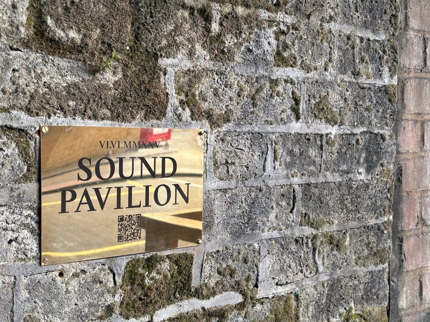 A plaque against a brick wall showing a QR code and the words 'sound pavillion'
