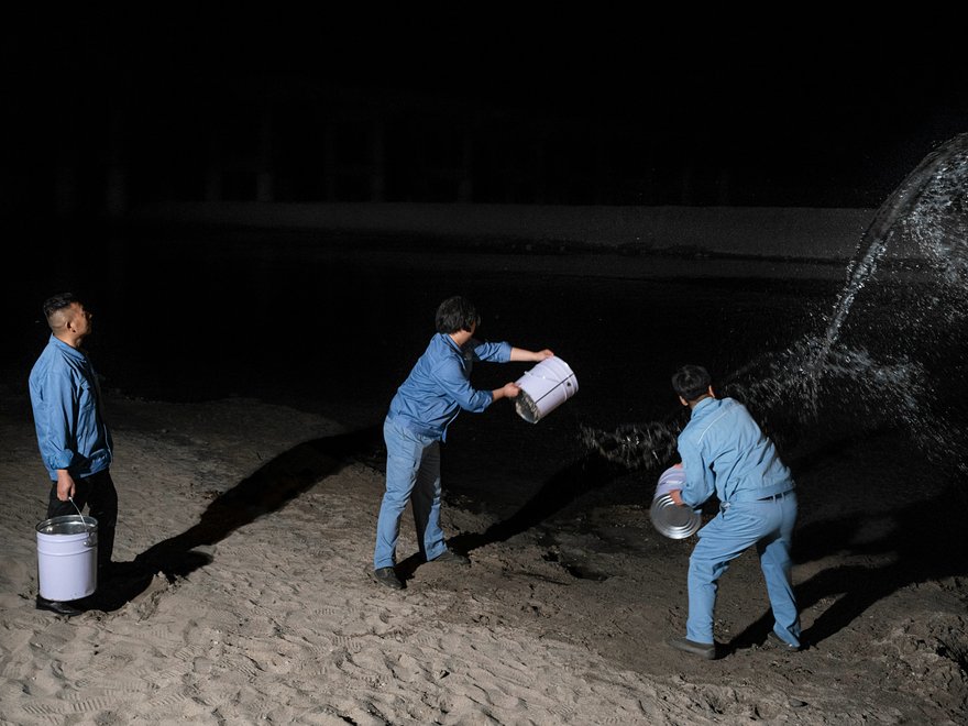 a photograph of three men on a beach at night throwing water into the sea