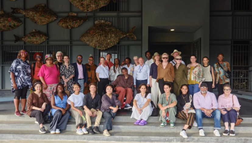 A group image of people sat on steps with large papier mache fish behind