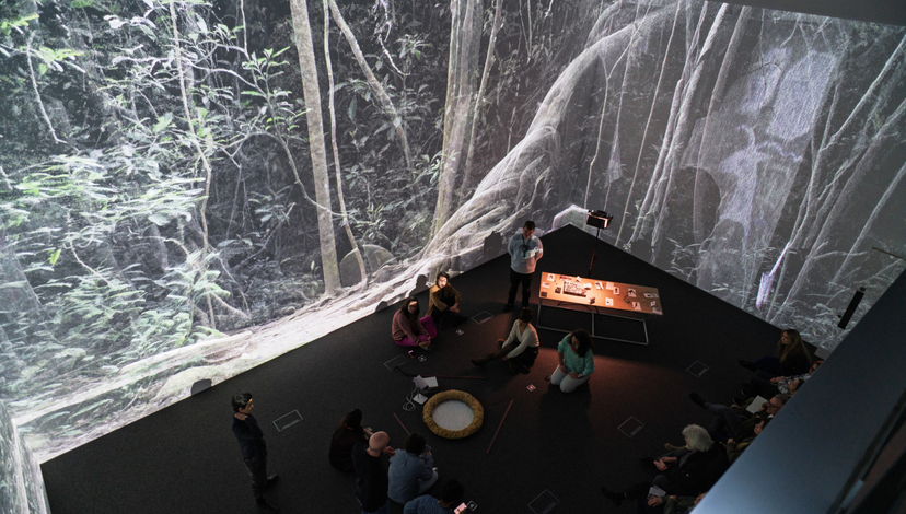 People sitting on the floor of a dark room with images of a forest being projected onto the walls